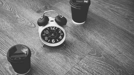 Top view of retro alarm clock, cappuccino in plastic glasses, aromatic American coffee, black and white image.の写真素材