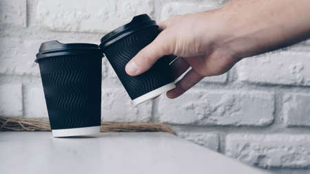 A man makes a coffee toast, a glass of coffee, cappuccino in his hand, black coffee in a plastic glass, close-up, black and white photo.Against the background of a brick wallの写真素材