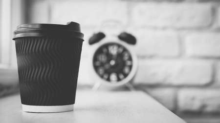 Close-up of cappuccino in a glass against a white brick wall background, in the background beautiful yellow retro clock with an alarm clock, black coffee on the bar counter. Black and white picture.の写真素材