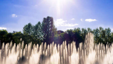 A beautiful fountain on the background of trees and green foliage, blue sky, water flooding, close-up.の写真素材