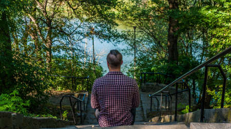 A man sits on the steps and thinks about something, a sad guy in a park, a thinking young man.View...