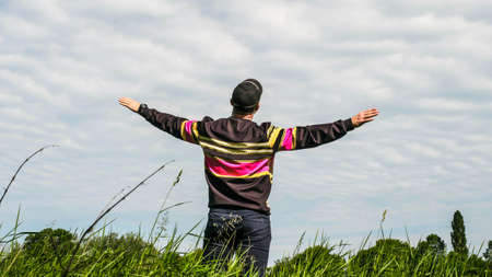A man stands in nature in a green meadow field and holds his hands to the sides, a man pretends to...