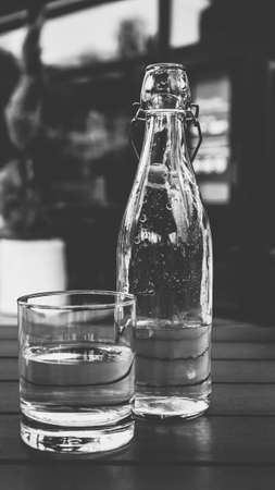 Mineral water in a glass and a bottle on a wooden table black and white paintingの写真素材