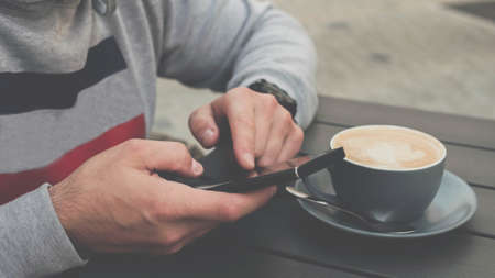 Man with a cup of coffee and a phone in his hands, the concept of drinking coffee in a cafe bar restaurant. Drink cappuccinoの写真素材