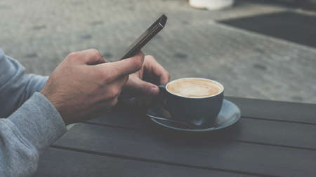 Drink cappuccino with smartphone, man is enjoying a cup of coffee in a restaurant in a cafeteria.