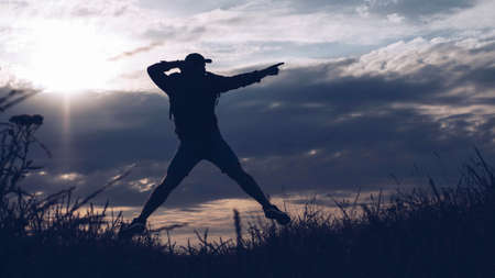 Silhouette of a guy in a jump at sunset, a young man in a jump and points his forefingerの写真素材