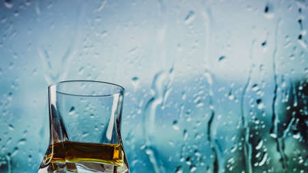 A glass of whiskey, whiskey on the bar by the window, drops trickling down the glass.の写真素材
