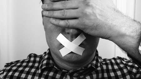 A man covers his eyes with his hand and mouth, a man with a closed face with objects. Sealed mouth with tape, duct tape.の写真素材