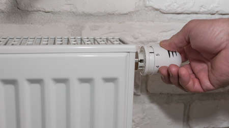 He adjusts the heating radiator, a man adjusts the hot water radiator, close-up of the radiator in...