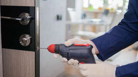 A carpenter repairs an interior door, a craftsman with an electric drill in his hands.