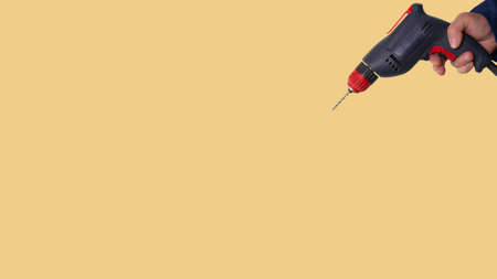An electric drill in a man's hand on a bright beautiful background, a construction tool on a yellow background.の写真素材