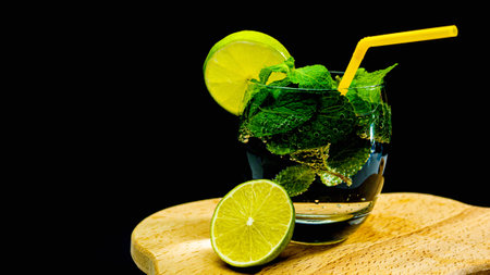 Mojito alcoholic cocktail on a black background. Mint drink in a glass with a straw and lime. Summer...