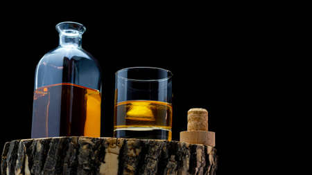Whiskey bottle on a wooden board with a glass filled with ice whiskey on a black background.の写真素材