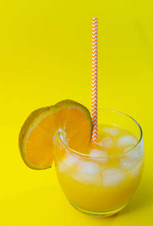 Yellow lemonade with ice in a glass. Fruit cocktail, orange juice with a straw in a glass. A glass with a straw and juice.の写真素材