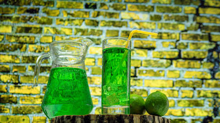 Fruit green drink in a glass against a brick wall background, green lemonade in a glass with lime. Summer drink with ice.の写真素材