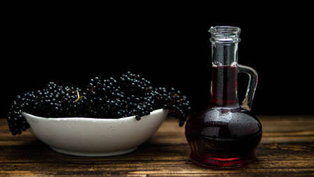 Elderberry in a plate on a wooden table on a black background, elderberry tincture in a bottle. Berry medicine.の写真素材