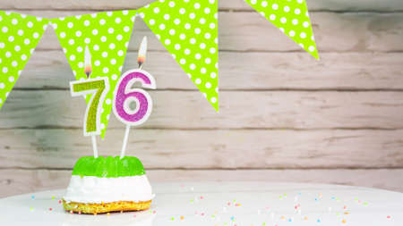 Beautiful festive background with the number 76 with a cake and lit candles, space saving for any holiday. Garland with birthday decorations for a postcard.Decorations are multi-coの写真素材