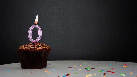 Muffin on black with a number from a candle number 0. Copy space, a pie on a black background, a card for congratulations on your birthday, anniversary.の写真素材