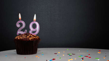 Muffin on black with a number from a candle number 29. Copy space, a pie on a black background, a card for congratulations on your birthday, anniversary.の写真素材