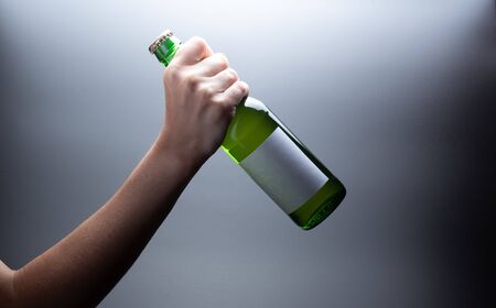 Tilted bottle of green glass with a label in the female hand on a dark backgroundの写真素材