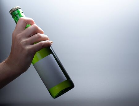 A tilted bottle of green glass that holds a female hand on a dark backgroundの写真素材