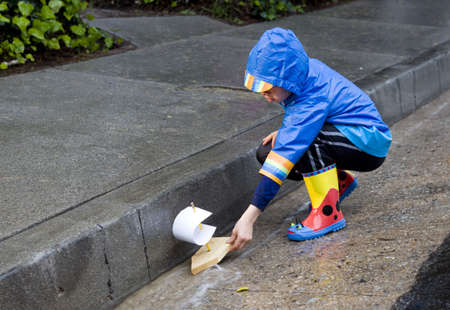 Young boy playing with toy boat in the rain wearing rain slickers and golashes.の写真素材