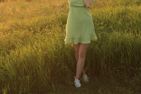 Young woman in green dress standing on green grass at sunset. back viewの写真素材