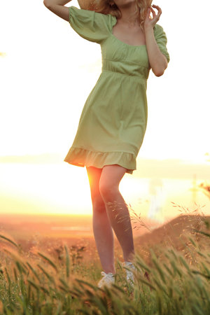 Beautiful young woman in a green dress on the field at sunsetの写真素材