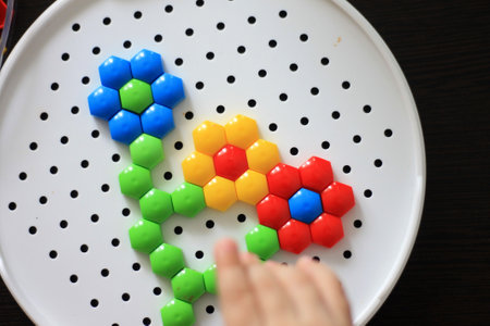 Children's hand playing with colorful plastic blocks on a white plate.の写真素材