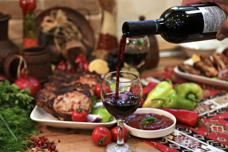 Pouring red wine from bottle into glass on table with vegetables and meatの写真素材