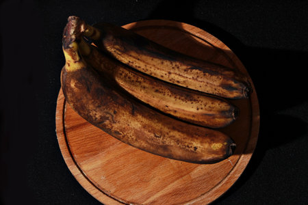 Ripe bananas on a wooden plate on a black background. Black background.の写真素材