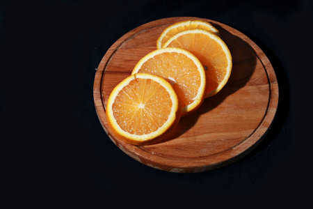 Slices of orange on a wooden plate on a black backgroundの写真素材