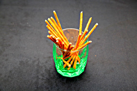 Crispy bread sticks in a glass on a black background.