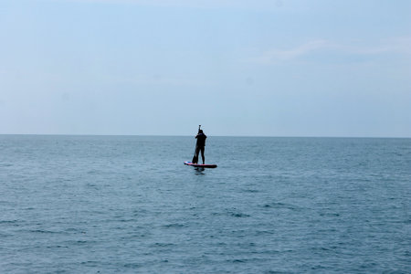 A man standing on a stand up paddle board in the sea.の写真素材