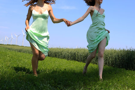 Two young women holding hands and running on the green meadow.の写真素材