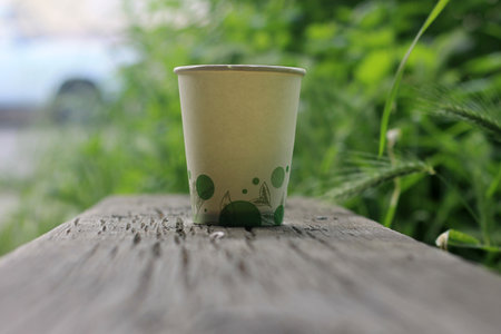Paper cup of coffee on the wooden table in the garden with grass backgroundの写真素材