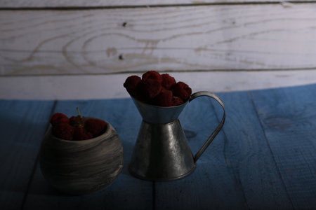 Still life with fresh raspberries in a metal jug on a wooden background