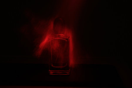 Glass of perfume on a dark background with red light and fog.の写真素材