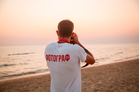 Young man taking photo with mobile phone on the beach at sunset.の写真素材