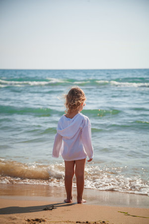 Little girl standing on the beach and looking at the sea in summerの写真素材