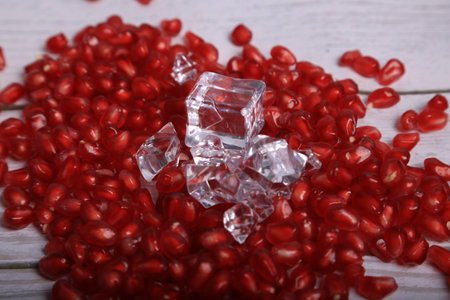 Ripe pomegranate seeds and ice cubes on wooden backgroundの写真素材