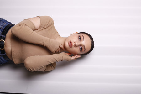 Young woman lying on the floor, leaning against a white wall.の写真素材