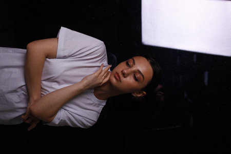Young woman sleeping on the windowsill in the dark room, vertical