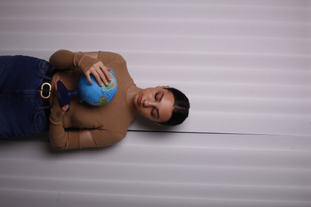 Young woman lying on the floor and holding a globe in her handの写真素材