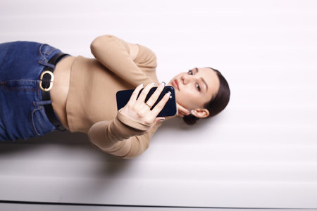 Young woman lying on the floor and using a mobile phone. Indoors.