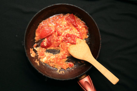 stewed tomatoes in a pan with a wooden spoon on a black backgroundの写真素材