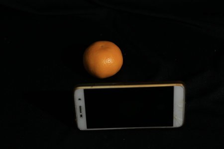 Orange and mobile phone on a black background with a black screen.