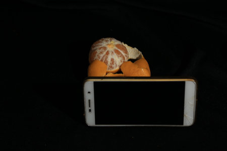 Mobile phone and tangerine on a black background, close up