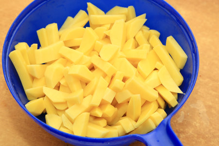 Sliced potatoes in a blue colander on a wooden backgroundの写真素材
