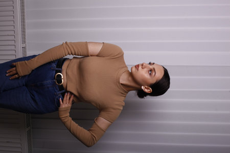 Young beautiful woman in jeans and beige sweater posing against the wallの写真素材
